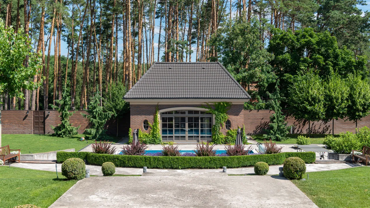 Działka z basenem, tarasem i wolno stojącym budynkiem gospodarczym na tle sosnowego lasu