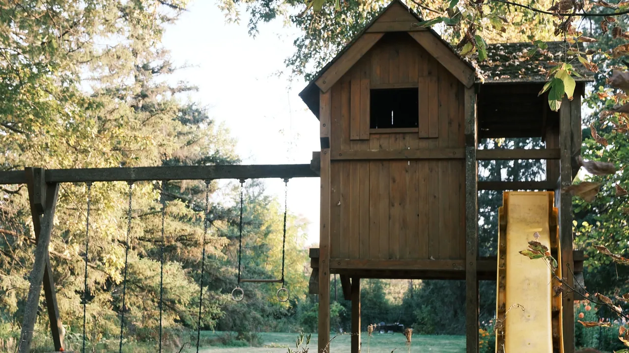 Drewniany domek na palach ze zjeżdżalnią i huśtawkami, ustawiony w ogrodzie