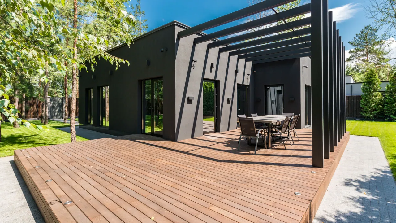 Aluminiowa pergola z regulowanymi lamelami nad drewnianym tarasem przy ciemnym domu
